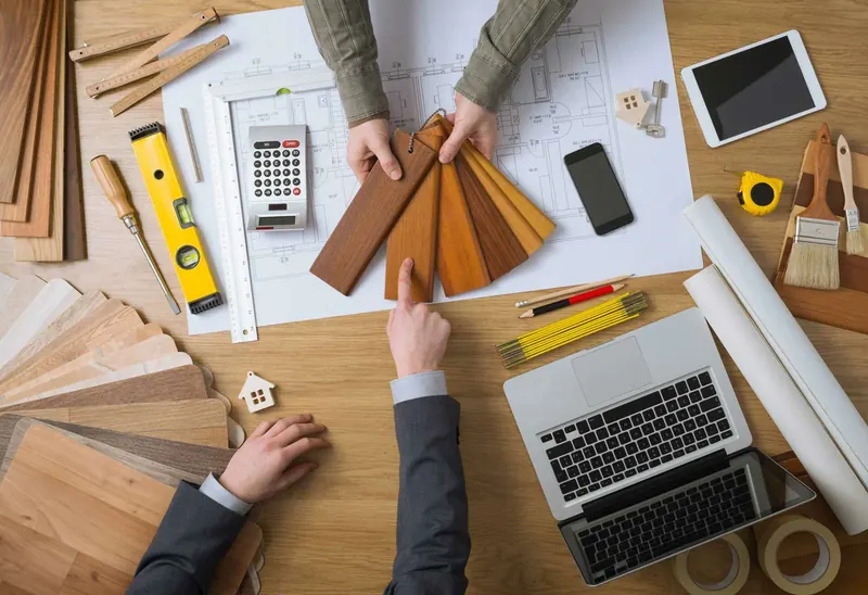 Planos, muestras de madera y herramientas sobre una mesa de trabajo
